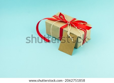 New Year's gift packed in kraft paper with red satin ribbon and a card for congratulations. blue background