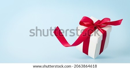 White gift box with red ribbon over blue background. With space for your Christmas, birthday or Valentines day greetings