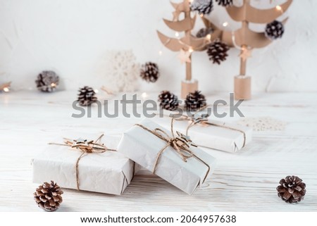 Christmas gifts wrapped in craft paper tied with twine on the background of Christmas fir trees made of cardboard on a wooden table. Organization of an eco-friendly holiday. Copy space