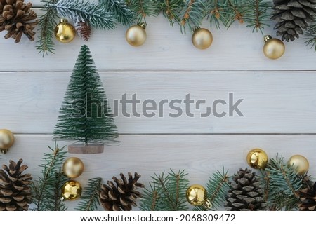 Top view of toy pine tree, golden christmas balls, pine tree branches and cones on white wooden background, copy space. Christmas decoration                                                    