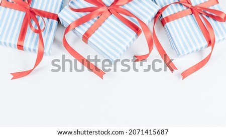 Three gift boxes in blue stripes with red ribbons lie on a white background with space for text from below, close-up top view. Christmas and New Year concept.