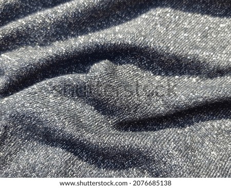 Wavy black shiny fabric with machine knit and lurex, in folds (macro, texture).
