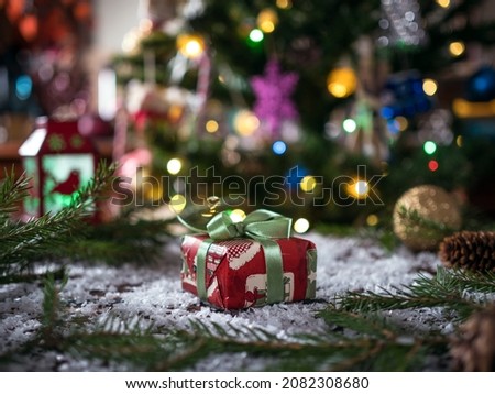 A beautifully wrapped Christmas present under the tree with defocused lights in the background. Christmas background.