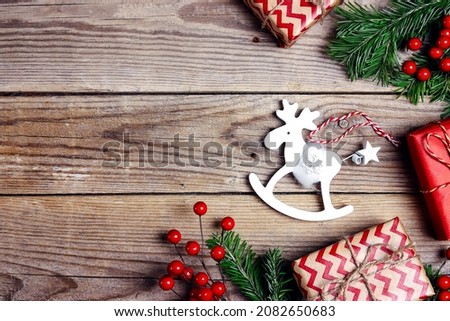 Christmas background with toy elk, gifts, fir branches and red berries on a wooden table. Top view border with copy space.
