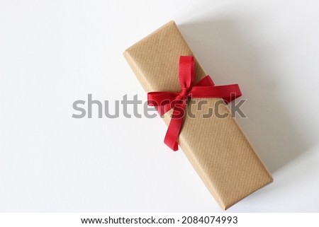 Christmas Gift Box Wrapped in Brown Kraft Paper and Decorated with Red Ribbon on White Background.