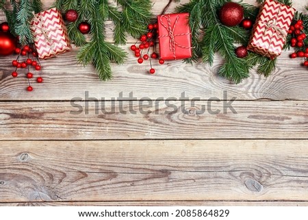 Christmas border from fir branches, berries and gifts on wooden background. Copy space, top view.