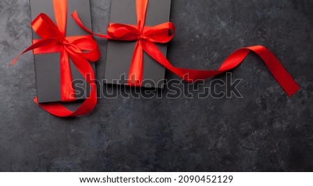 Two black gift boxes with red ribbon on stone background. Top view flat lay with copy space
