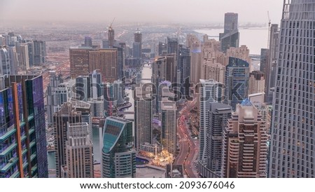 Skyline panoramic view of Dubai Marina and JBR showing canal surrounded by illuminated skyscrapers along shoreline aerial day to night transition. Traffic on curved road after sunset. DUBAI, UAE