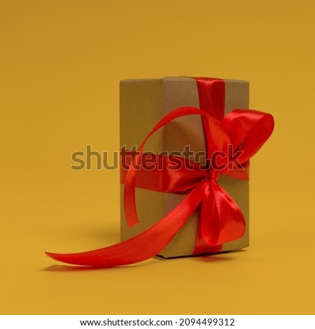 gift wrapped in craft paper with red ribbon on yellow background, close-up
