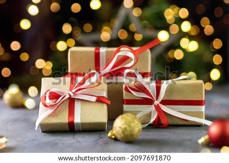 Christmas gift in craft paper with white and red ribbon and Christmas tree on dark background with star and golden bokeh. Merry Christmas and happy New year.