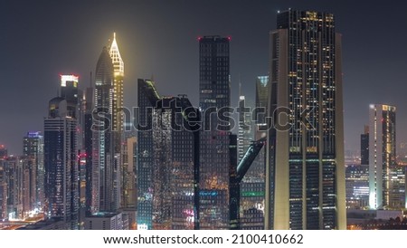 Close up view of Dubai Financial Center district with tall skyscrapers illuminated during all night timelapse with lights turning off. Aerial view to towers along busy highway