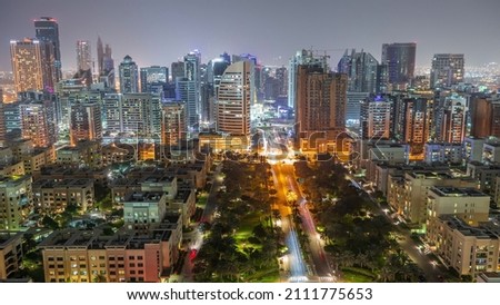 Skyscrapers in Barsha Heights district and low rise buildings in Greens district aerial night timelapse. Dubai skyline with palms and trees nead road with traffic