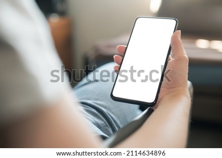 Young woman sitting in chair and holding smartphone with white screen