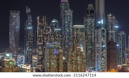 Skyscrapers of Dubai Marina with illuminated highest residential buildings with glowing and blinking windows during all night timelapse. Aerial top view from JLT district