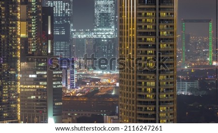 Towers in Dubai International Financial Centre district aerial night timelapse. Office buildings and hotels with modern skyscrapers under construction and traffic on overpass