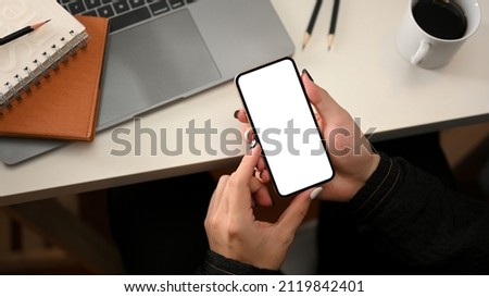 Top view of a female using modern smartphone white screen mockup over modern workspace.