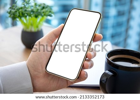 male hand holding phone with isolated screen on background of table in office 
