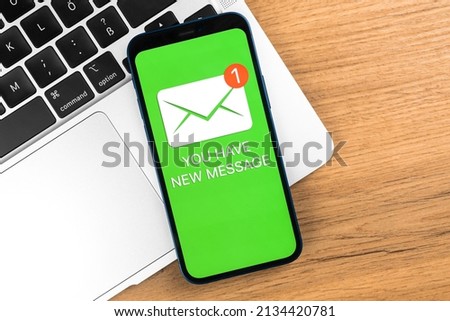 Smartphone and new message icon. Business workplace background with laptop on a wooden table, top view