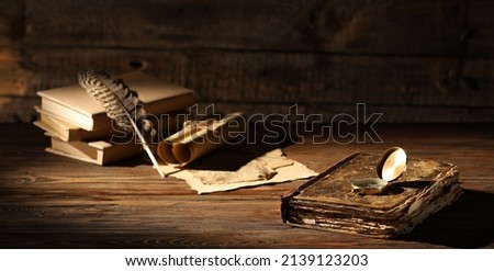 Old books with compass, feather and scrolls on wooden table 