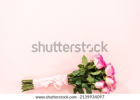 Bouquet of pink roses wrapped in pink wrapping paper with a pink ribbon on a pink background.