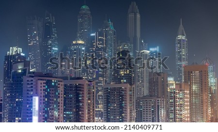 Dubai marina tallest block of skyscrapers with glowing windows night timelapse. Aerial view from JLT district to apartment buildings, hotels and office towers near highway.