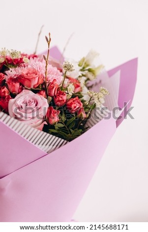 There is a interesting bouquet of wonderful flowers. The bouquet is in a purple-white wrapper on the white background. It is a great present for somebody. It is ready to be bought to the customers.