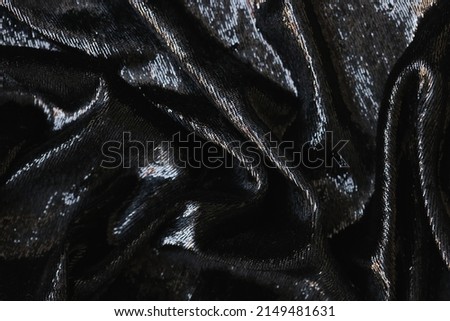 Closeup of tousled shiny black silk fabric. Black texture fabric background