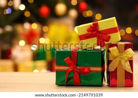 Beautifully wrapped gift boxes on wooden table against blurred festive lights, space for text. Christmas celebration