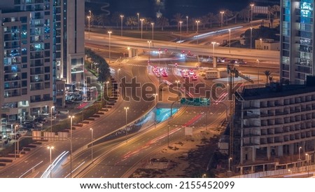 Huge highway crossroad junction with tunnel near JLT district aerial night timelapse. Golf course near illuminated towers and skyscrapers with busy traffic and construction site