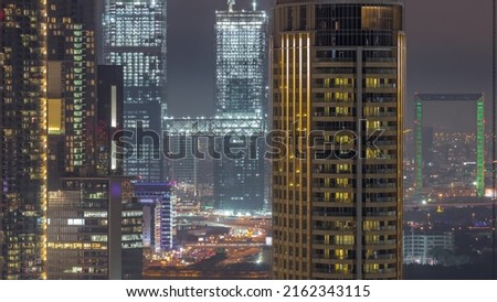 Towers in Dubai International Financial Centre district aerial night timelapse. Office buildings and hotels with modern skyscrapers under construction and traffic on overpass