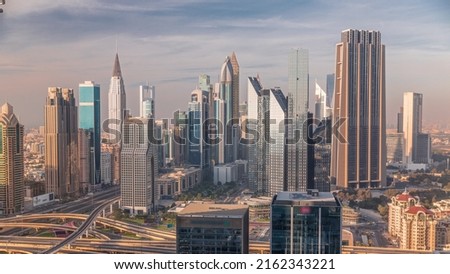 Panorama of Dubai Financial Center district with tall skyscrapers timelapse. Aerial view to towers along busy highway during sunset