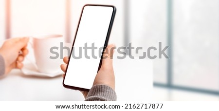 Mockup image of woman's hand holding black mobile phone with blank screen while drinking coffee. woman using cell phone mockup while drinking coffee in modern cafe