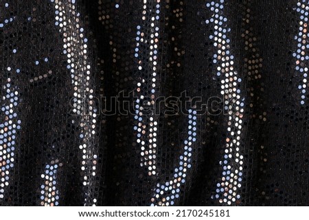 Top view of black cloth with colourful sequins abstract background. Stylish wavy fabric texture backdrop