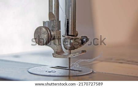 Close-up of the needle of an old sewing machine with a white thread tucked in. The concept of repair, tailoring.