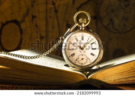 Antique pocket watch on opened old book. Old map on background.