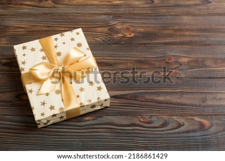 wrapped Christmas or other holiday handmade present in white paper with gold ribbon on colored background. Present box, decoration of gift on colored table, top view with copy space.