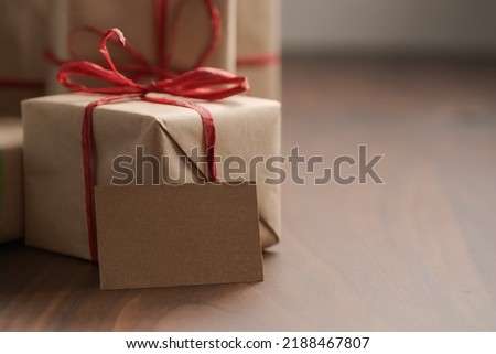Brown paper gift boxes with red bow and blank paper card on walnut table with copy space, shallow focus