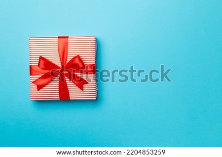 Gift box with red ribbon bow on color background, top view.