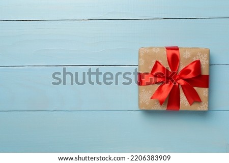 Gift box with red ribbon bow on wooden background, top view.