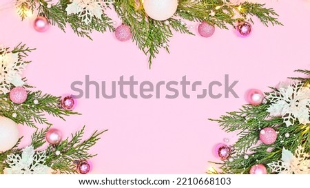 Pastel pink background with copy space and pine branches decorated with white flowers and pink ornaments. Flat lay