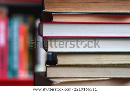 Stack of colorful hardcover books and reading glasses in front of a bookshelf. Selective focus.