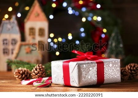 Christmas present. Beautiful gift box, cones and candy canes on wooden table against blurred festive lights, space for text