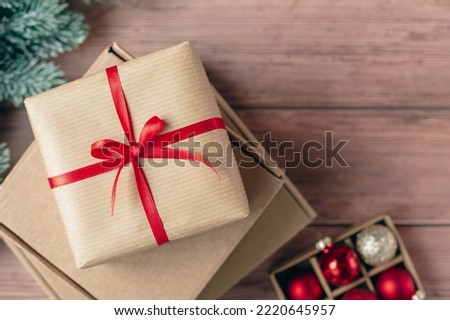 Gift cardboard boxes for Christmas celebration with decorative red ribbon and red glass balls are on wooden background. Handmade gift for Christmas and New Year. View from the top point.