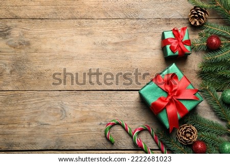 Gift boxes, candy canes, fir tree branches and Christmas decor on wooden table, flat lay. Space for text