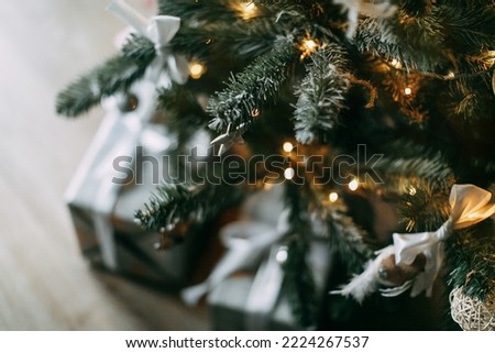 Christmas tree with beautiful, blurred light with stack of wrapped Christmas presents in silver tone under. Gift boxes in cozy home. Holiday eve atmosphere. Surprise for family and friends
