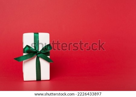 Gift box with green ribbon bow on color background.