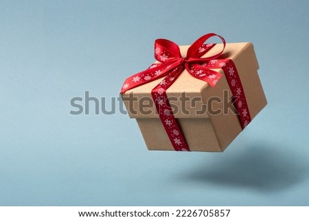 Flying Christmas gift box with red bow on blue background.