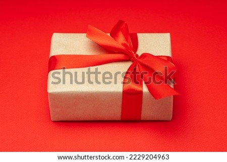Close up shot of gift box wrapped in craft paper and decorated with satin ribbon bow, isolated on red background.