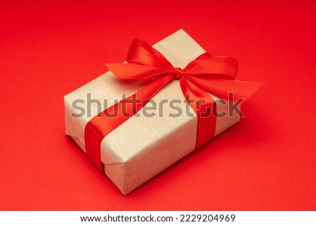 Close up shot of gift box wrapped in craft paper and decorated with satin ribbon bow, isolated on red background.