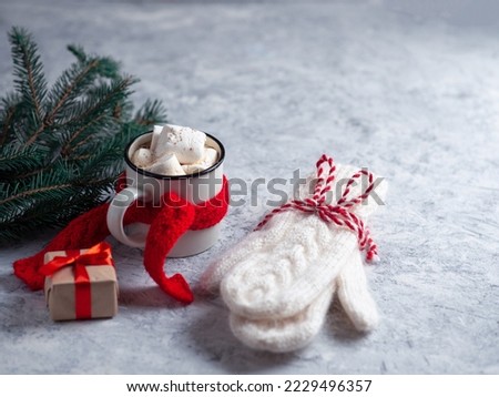 Hot chocolate or coffee with marshmallows on a white concrete table with Christmas tree branches, warm knitted mittens and a red scarf